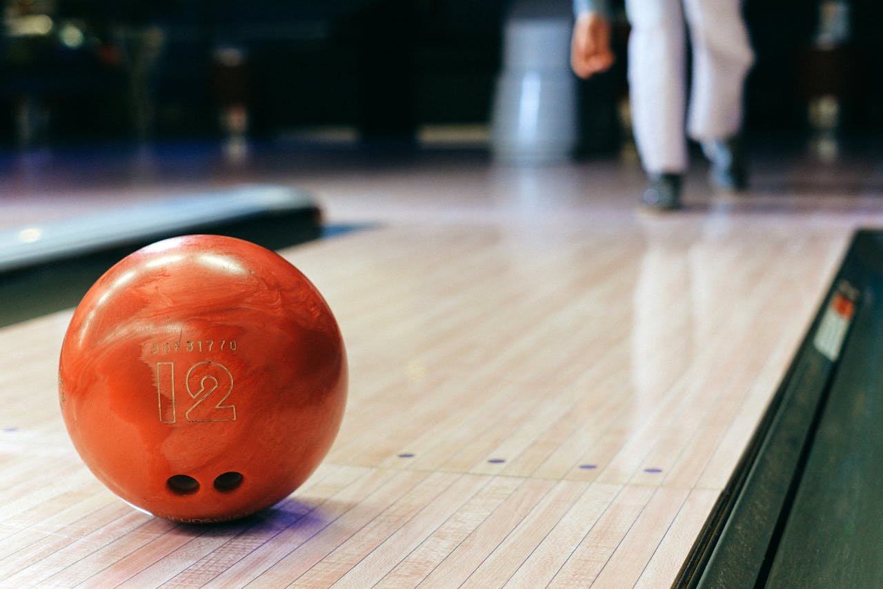 Close-up of a red bowling ball on a bowling alley lane with a bowler in the background.