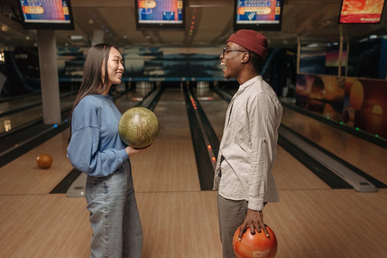 Friends enjoying a lively conversation while holding bowling balls at an indoor bowling alley.